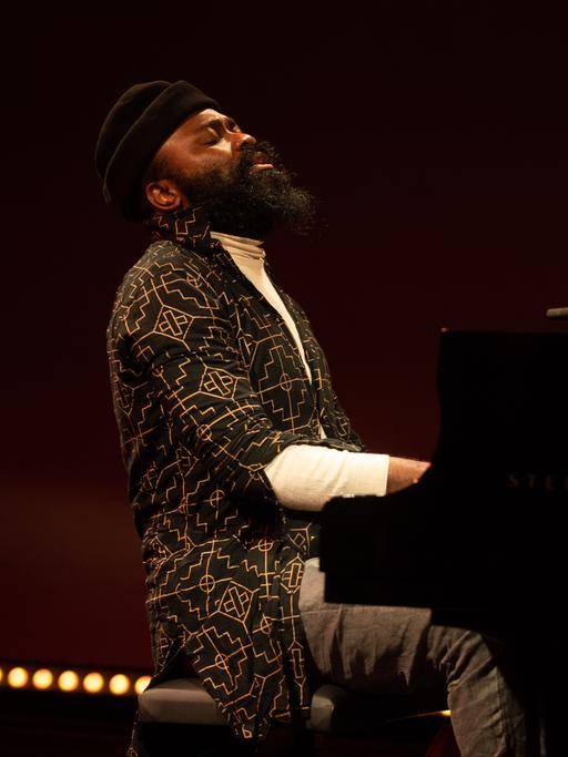 Ein bärtiger Mann mit schwarzer Wollmütze spielt zurückgelehnt mit geschlossenen Augen auf einer Bühne Klavier.