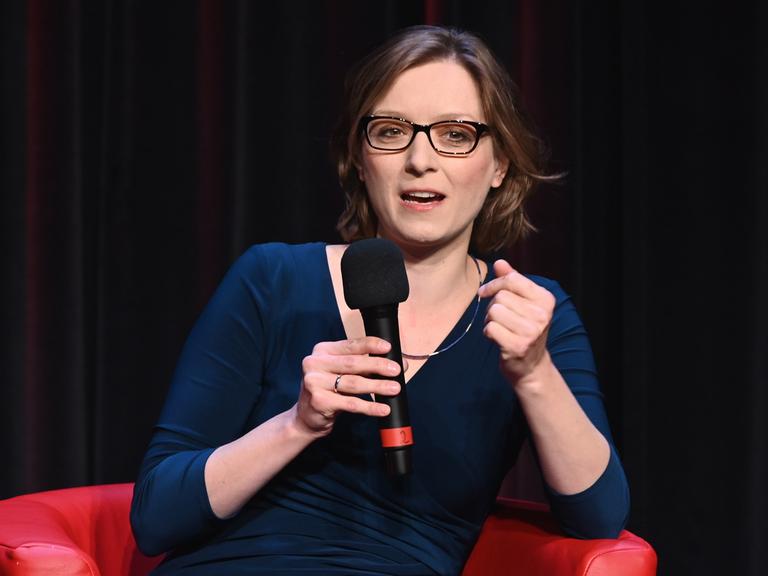 Die Philosophin Lisa Herzog sitzt auf einem Podium und spricht in ein Mikrofon.