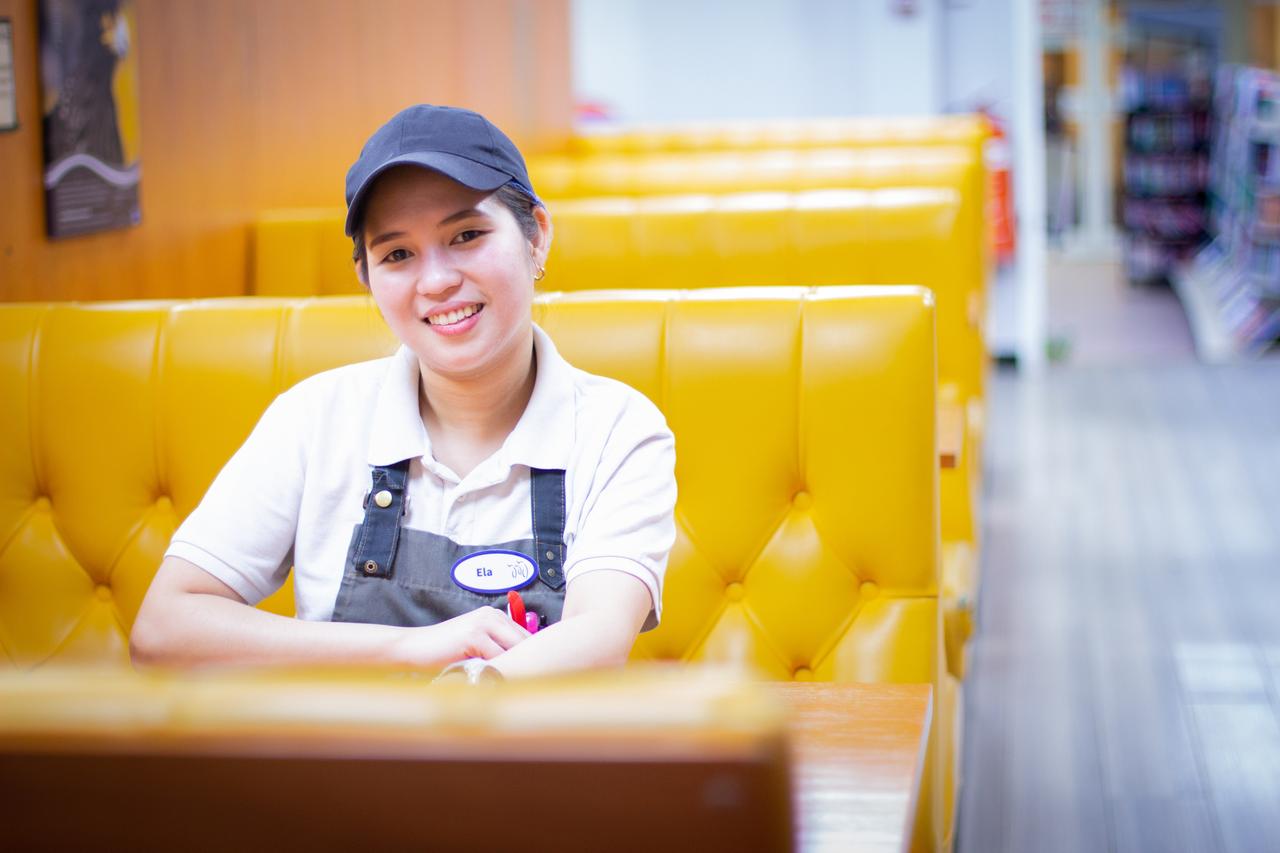 Eine junge Frau in Latz-Arbeitshose und Käppi sitzt lächelnd auf einem knallgelben Sitz.