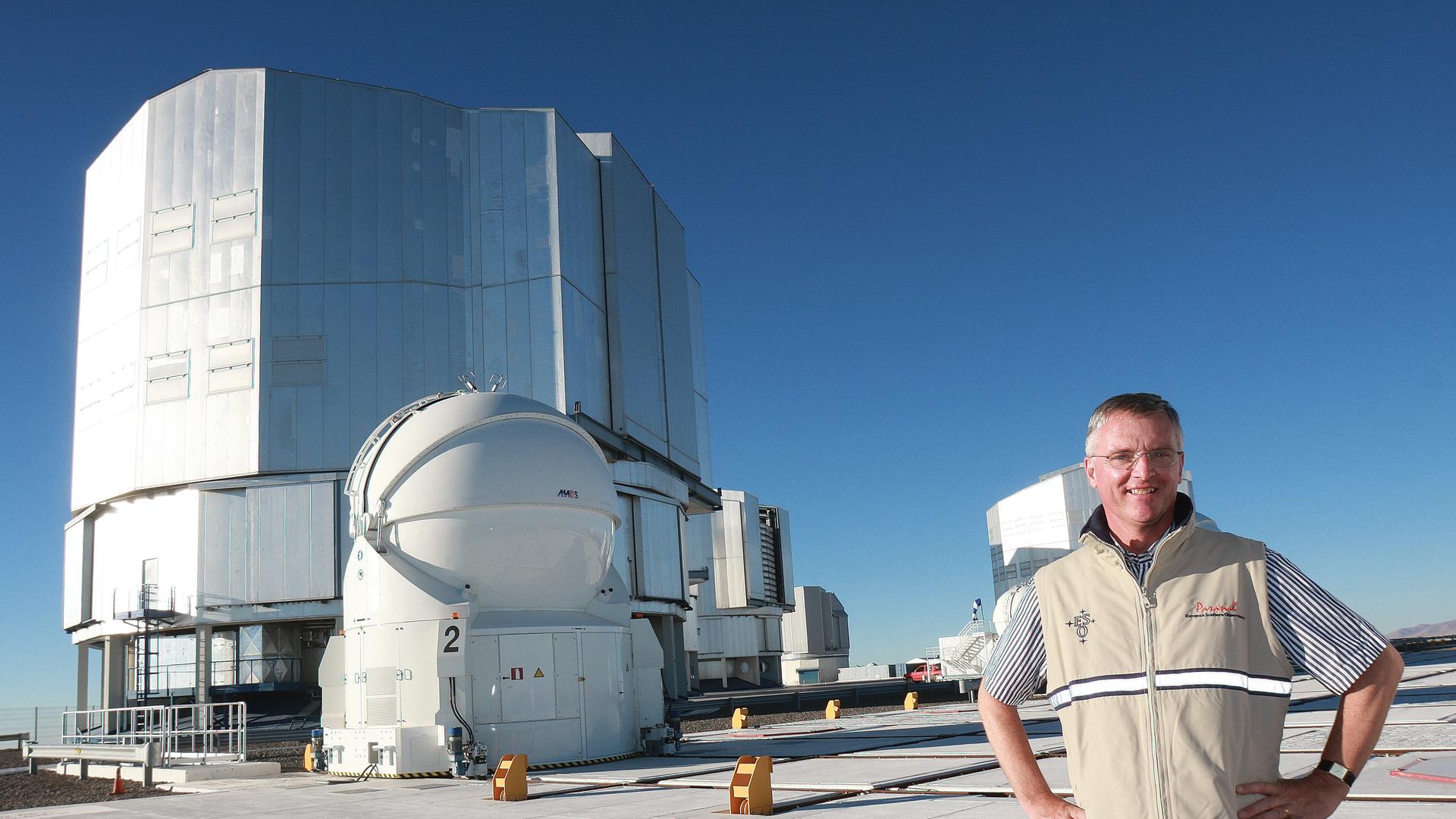 Professor Tim de Zeeuw, ESO Director General since September 2007, during a visit to the Paranal Observatory in August 2008. He stands on top of the Very Large Telescope platform in front of the enclosures of the four 8.2m unit telescopes ANTU, KUEYEN, MELIPAL, and YEPUN (from left to right). On the left the dome of AT2, one of the auxiliary telescopes, is seen. Professor Tim de Zeeuw, ESO Director General since September 2007, during a visit to the Paranal Observatory in August 2008. He stands on top of the Very Large Telescope platform in front of the enclosures of the four 8.2m unit telescopes ANTU, KUEYEN, MELIPAL, and YEPUN (from left to right). On the left the dome of AT2, one of the auxiliary telescopes, is seen.