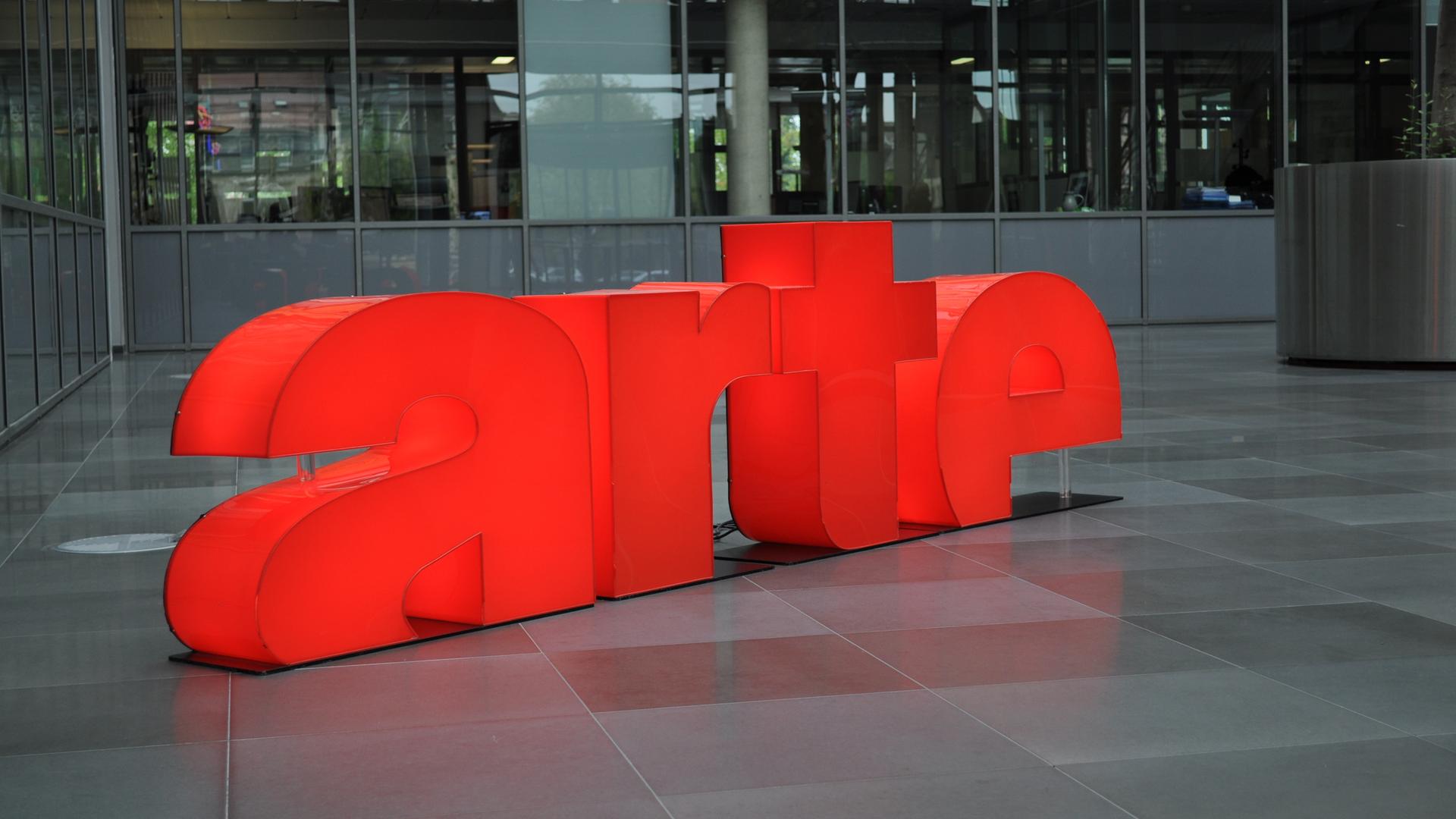 Am Sitz des deutsch-französischen Kultursenders Arte ist eine rote Skulptur mit dem Name des Sender aufgebaut. Im Hintergrund ist ein Bürogebäude. 