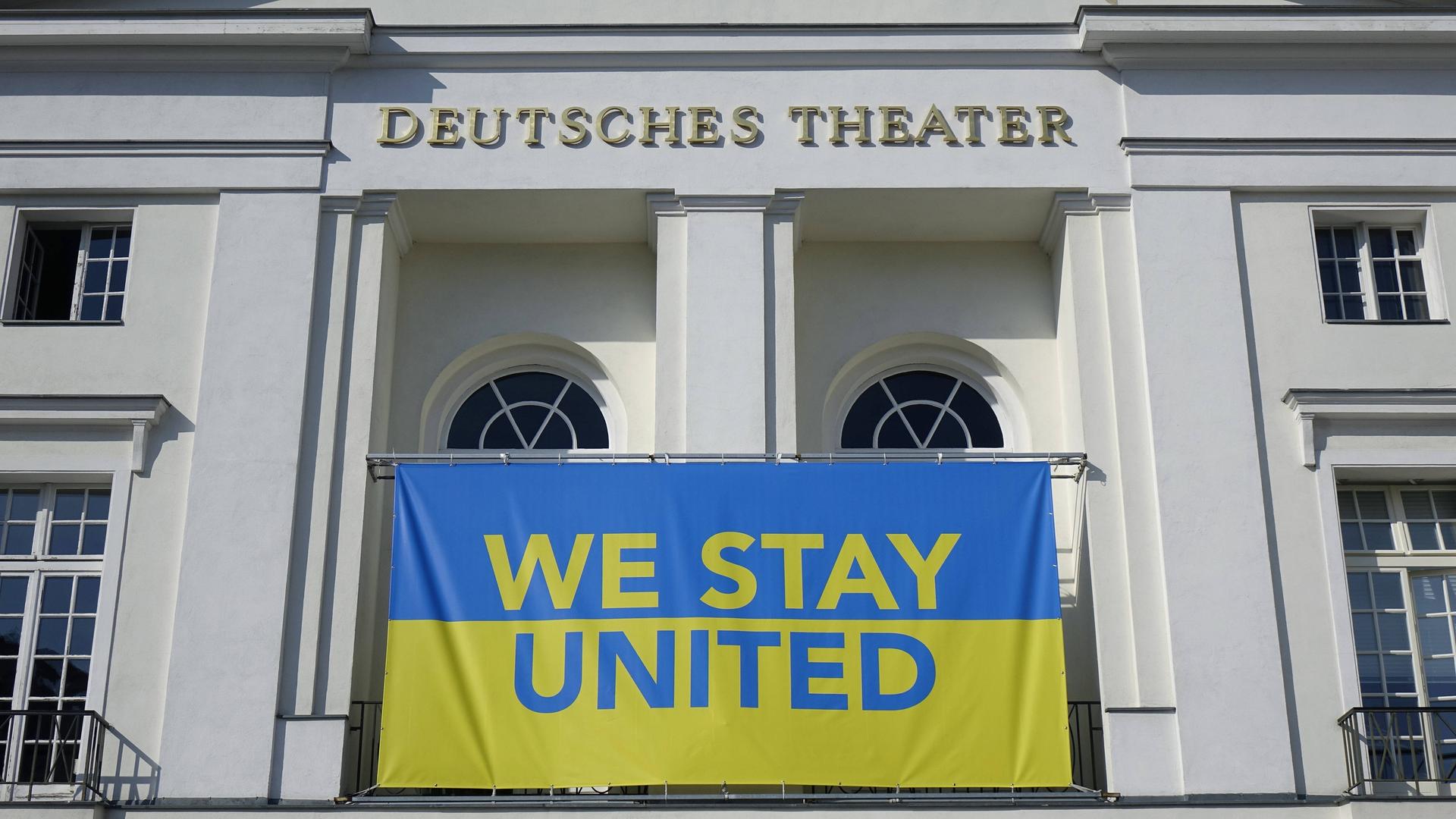 Die blau-gelbe Flagge der Ukraine mit der Aufschrift "We stay united" hängt am Deutschen Theater Berlin.