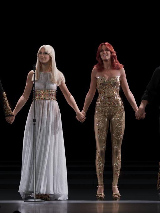 Die Avatare der Abba-Bandmitglieder Björn, Agnetha, Anni-Frid und Benny stehen nebeneinander auf der Bühne und halten einander an den Händen.