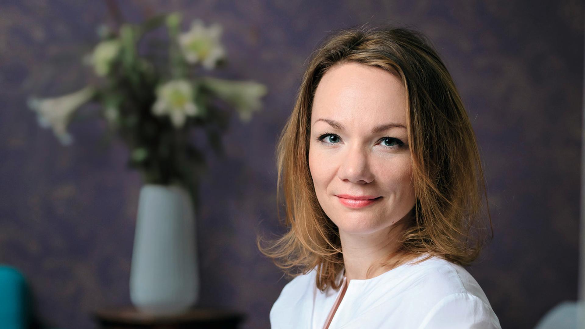 Sabrina Janesch sitzt auf einem grauen Sessel vor einer violetten Wand. Sabrina Janesch sitzt auf einem grauen Sessel vor einer violetten Wand.