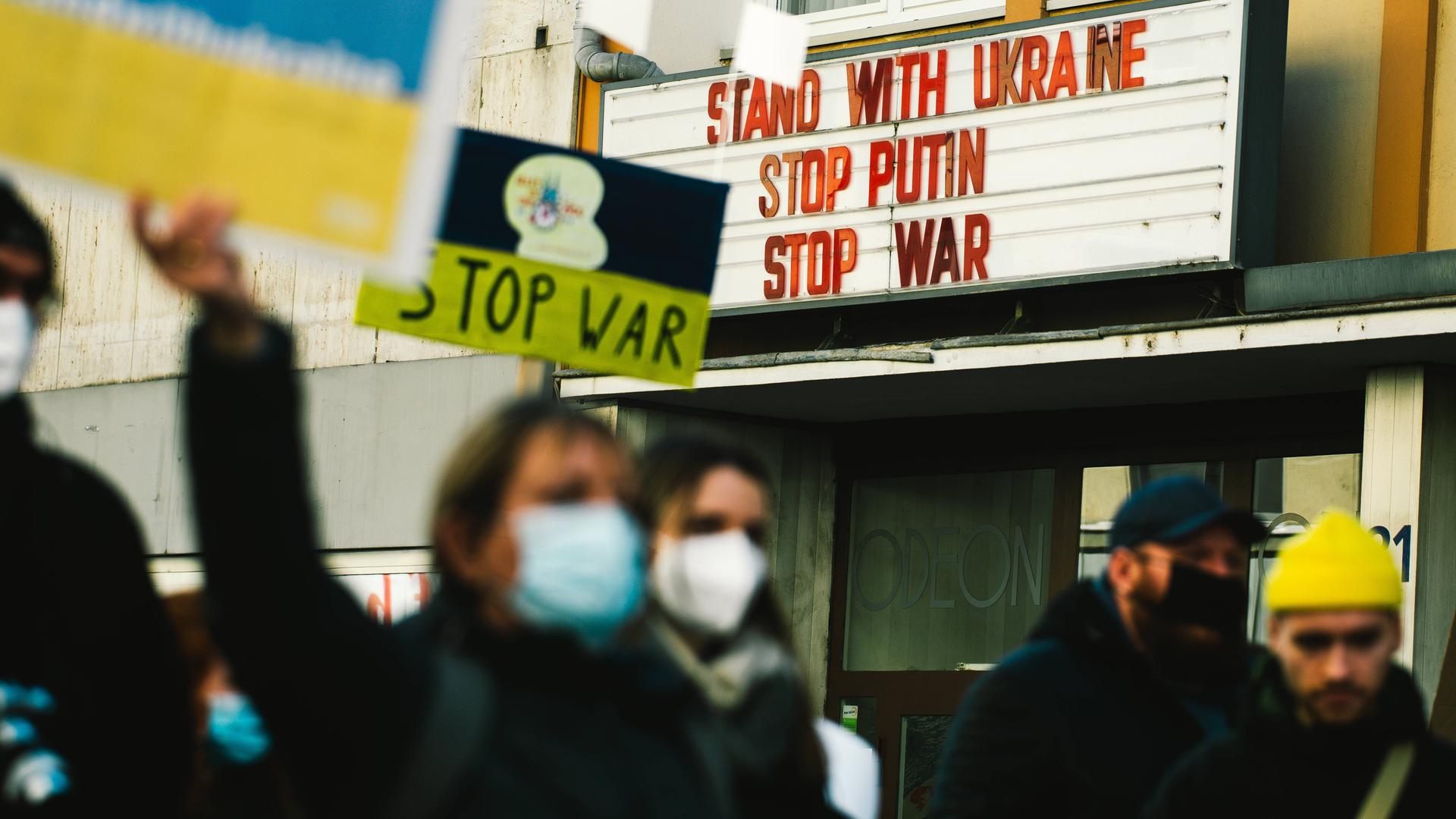 Demonstranten gehen an einem Kino vorbei. An dessen Hausfassade steht: Solidarität mit der Ukraine. Stoppt Putin. Stoppt den Krieg. Demonstranten gehen an einem Kino vorbei. An dessen Hausfassade steht: Solidarität mit der Ukraine. Stoppt Putin. Stoppt den Krieg.