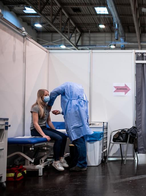 Eine Frau sitzt in einer Impfkabine im Impfzentrum in Essen und bekommt den Impfstoff von Biontech/Pfizer gespritzt. 