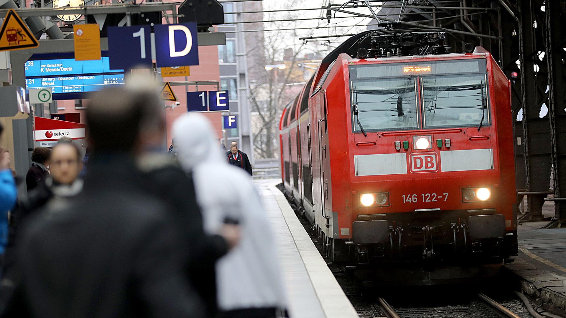 Ein Regionalexpress fährt in den Hauptbahnhof Köln ein, Menschen warten am Gleis.