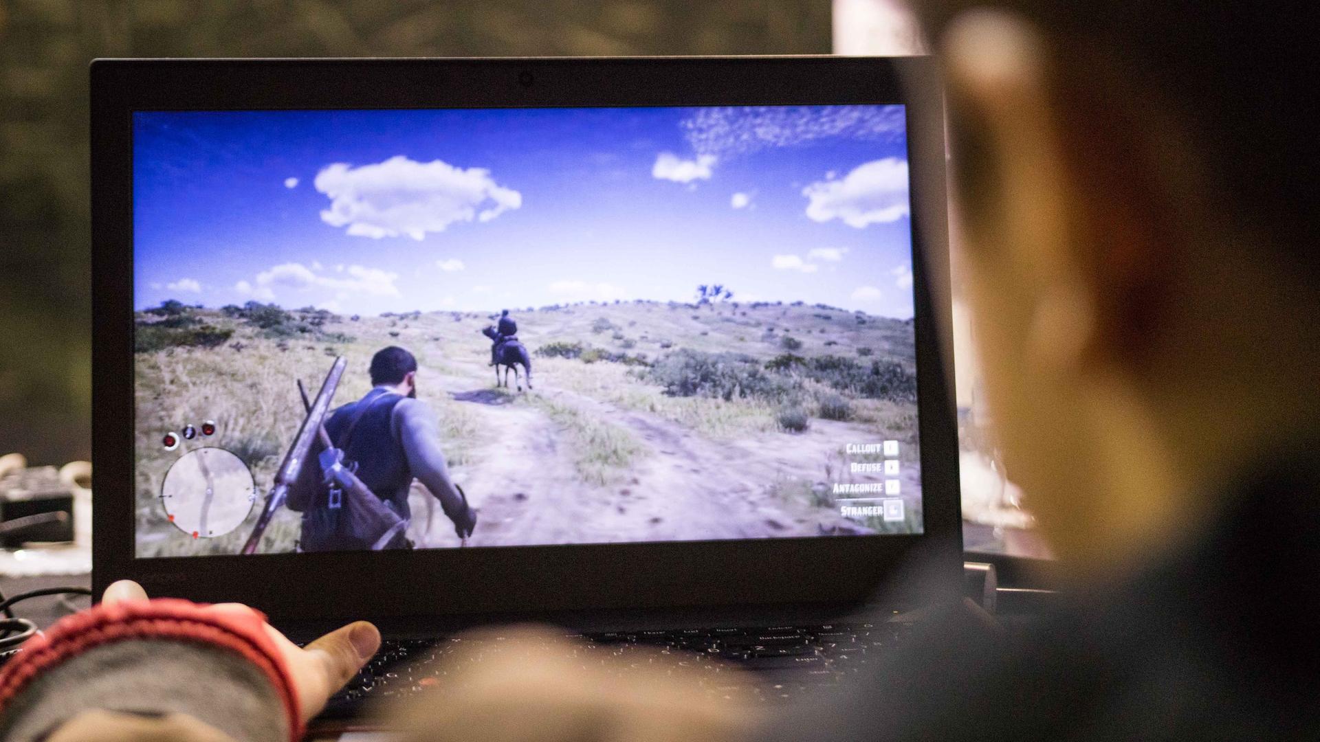 Eine Person sitzt an einem Computer und spielt Red Dead Redemption. Auf dem Bildschirm wird eine Szene aus dem Spiel dargestellt. Eine Person sitzt an einem Computer und spielt Red Dead Redemption. Auf dem Bildschirm wird eine Szene aus dem Spiel dargestellt.