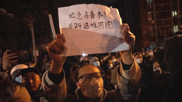 Bei einer Demonstration in Peking hält ein Mann mit Maske ein Schild hoch.