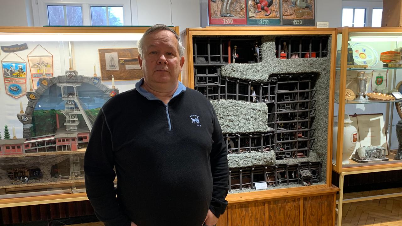 Hermann Meinel steht in blauem Pullover in seinem Uranmuseum in Bad Schlema. Hinter ihm Miniaturdarstellungen der Schächte vom Uranabbau hinter Glasvitrinen. Hermann Meinel steht in blauem Pullover in seinem Uranmuseum in Bad Schlema. Hinter ihm Miniaturdarstellungen der Schächte vom Uranabbau hinter Glasvitrinen.