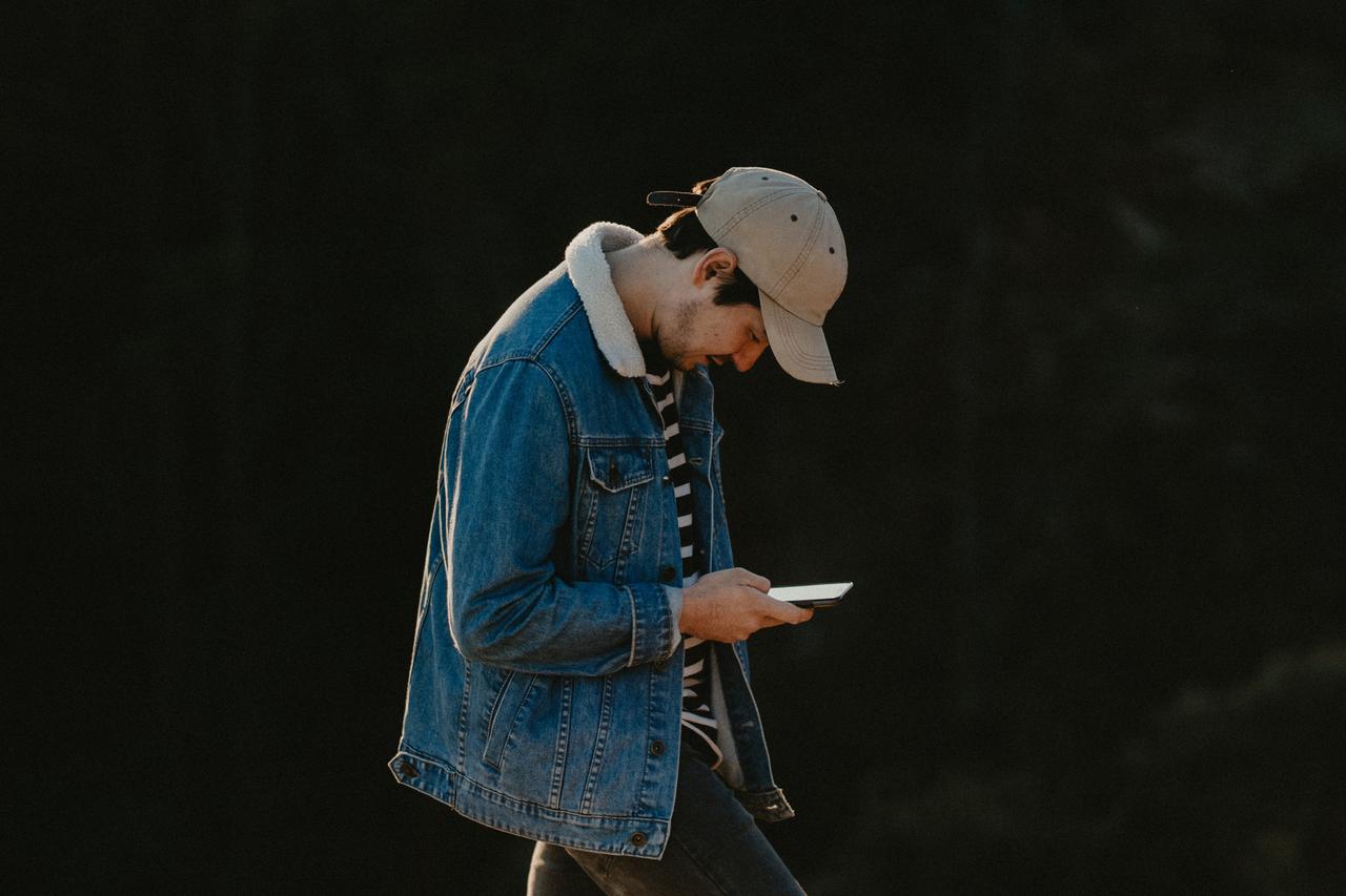 Ein junger Mann mit Käppi schaut im Laufen auf sein Smartphone Ein junger Mann mit Käppi schaut im Laufen auf sein Smartphone