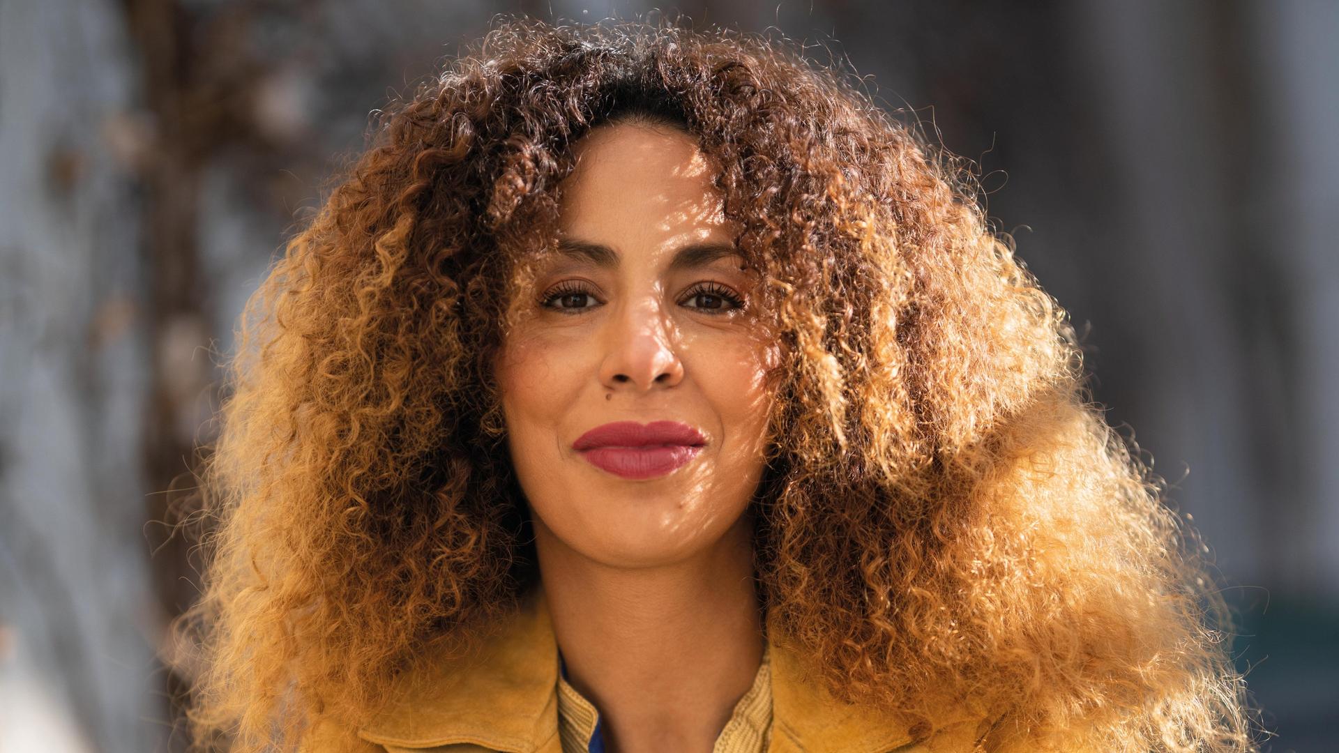 Die Integrationsexpertin Souad Lamroubal hat lange lockige Haare und blickt direkt in die Kamera, der Hintergrund des Fotos ist verschwommen. Die Integrationsexpertin Souad Lamroubal hat lange lockige Haare und blickt direkt in die Kamera, der Hintergrund des Fotos ist verschwommen.