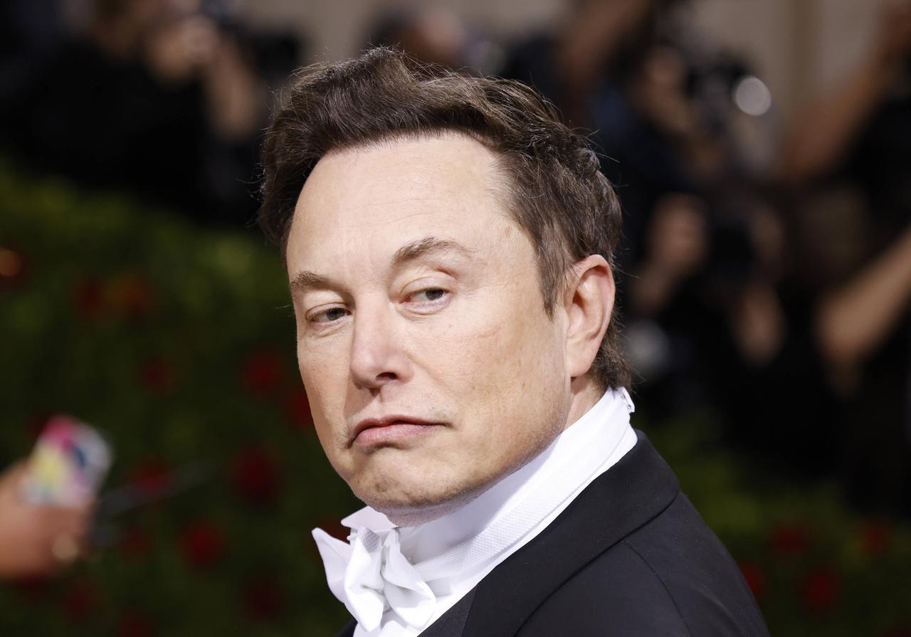 Elon Musk im schwarzen Anzug mit weißer Fliege schaut nach links über die Schulter.