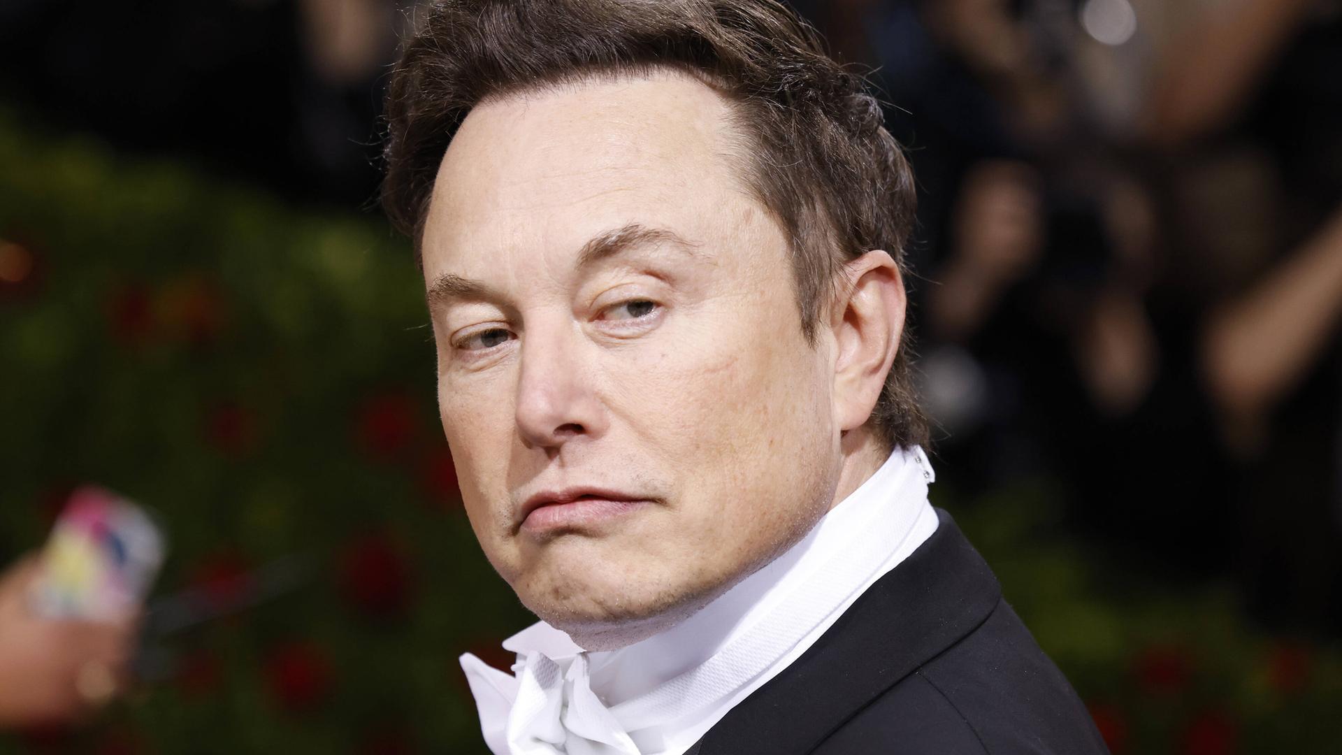 Elon Musk im schwarzen Anzug mit weißer Fliege schaut nach links über die Schulter. Elon Musk im schwarzen Anzug mit weißer Fliege schaut nach links über die Schulter.