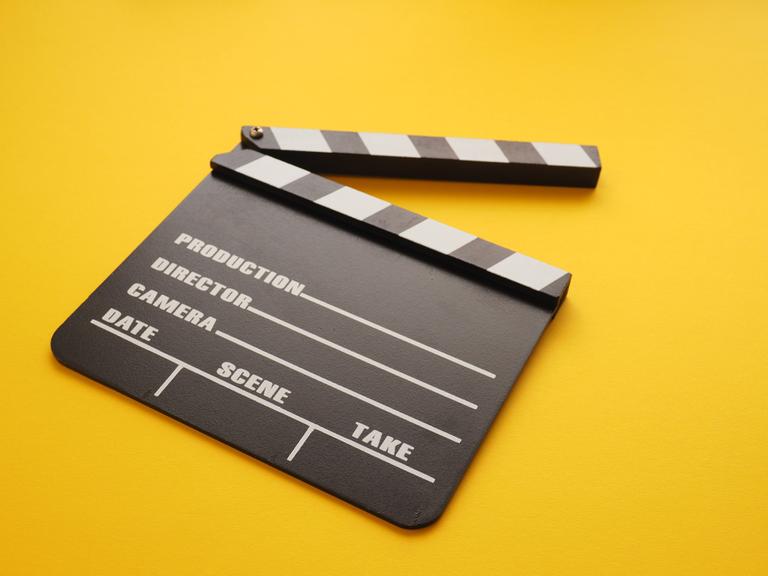Eine Filmklappe liegt auf einem gelben Hintergrund.
