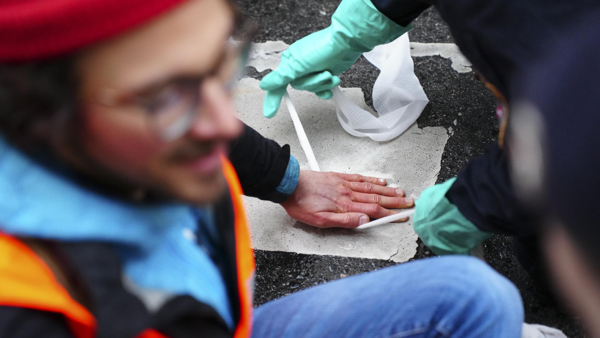 Ein junger Mann hat seine Hand auf den Asphalt geklebt. Jemand versucht sie, von der Straße zu lösen. Ein junger Mann hat seine Hand auf den Asphalt geklebt. Jemand versucht sie, von der Straße zu lösen.