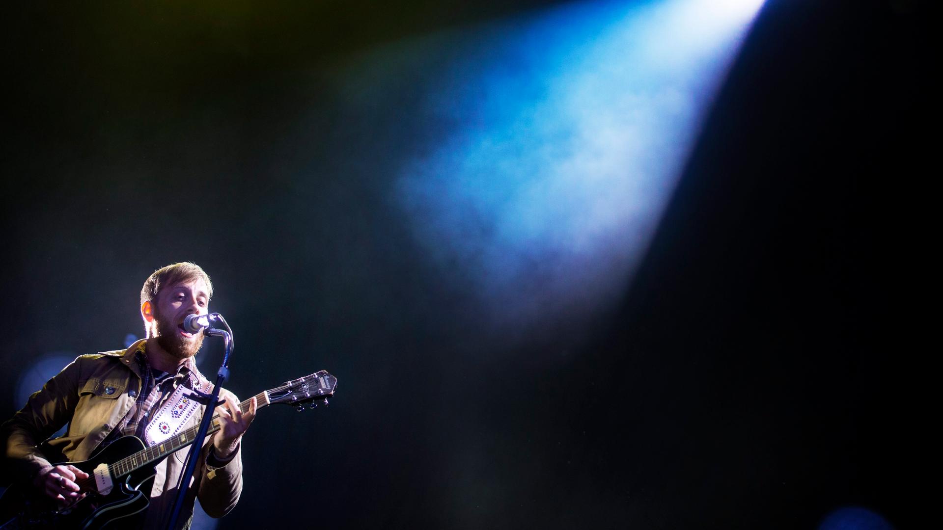 Dan Auerbach steht mit Gitarre  auf einer Bühne, die ein einziges Schlaglicht auf ihn wirft.