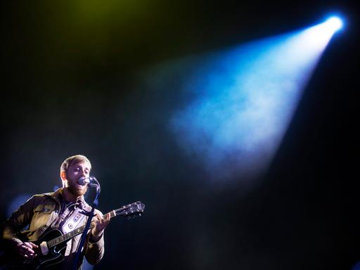Dan Auerbach steht mit Gitarre  auf einer Bühne, die ein einziges Schlaglicht auf ihn wirft.