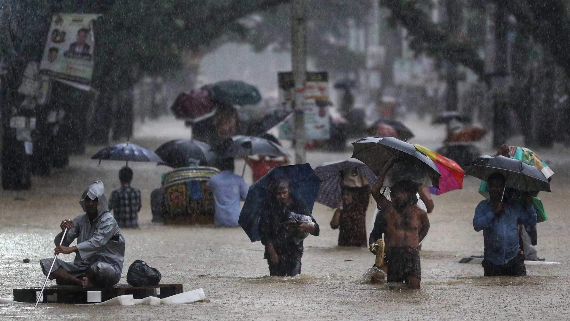 Menschen waten durch eine überschwemmte Straße in der Stadt Sylhet, Bangladesch. Menschen waten durch eine überschwemmte Straße in der Stadt Sylhet, Bangladesch.