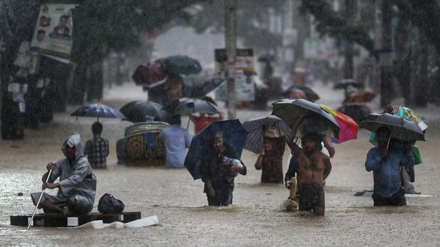 Menschen waten durch eine überschwemmte Straße in der Stadt Sylhet, Bangladesch.