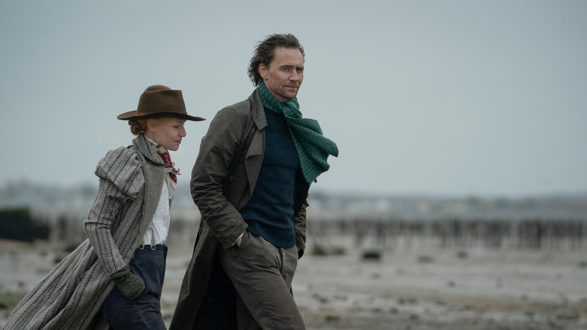 Ein Mann und eine Frau mit Hut spazieren am Strand.