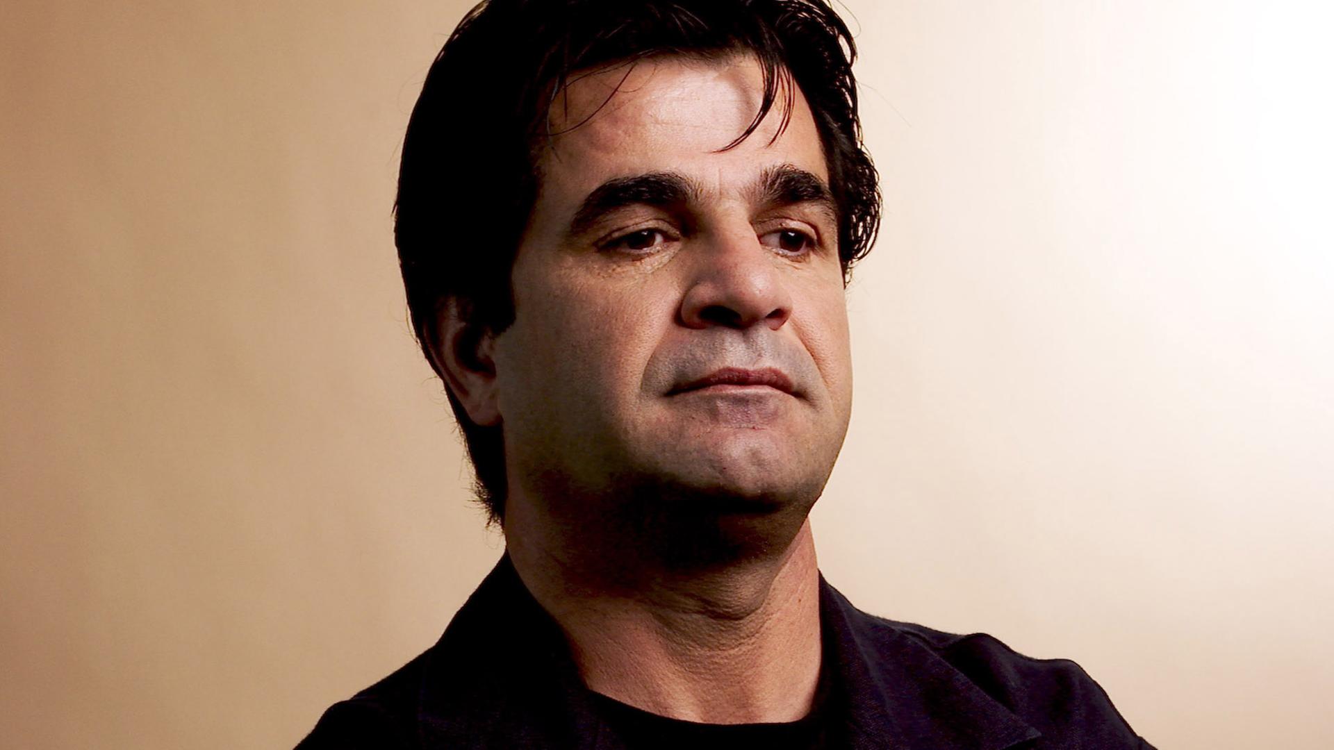 Porträt von Jafar Panahi mit verschränkten Armen und nachdenklichem Gesichtsausdruck. Porträt von Jafar Panahi mit verschränkten Armen und nachdenklichem Gesichtsausdruck.
