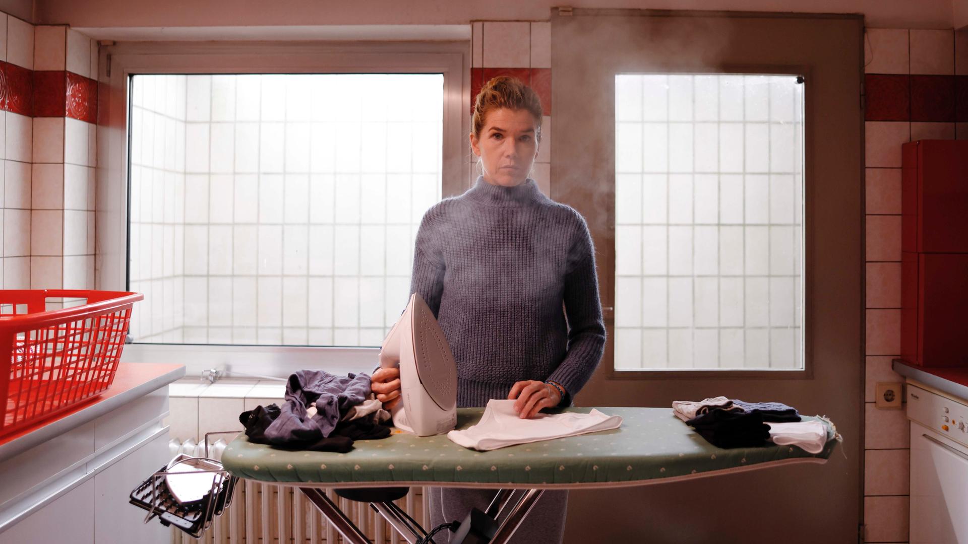 Anke Engelke steht mit einem dampfenden Bügeleisen am Bügelbrett (Szenenbild aus dem Film "Mutter")