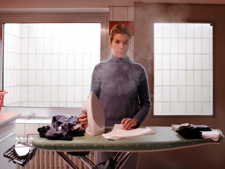 Anke Engelke steht mit einem dampfenden Bügeleisen am Bügelbrett (Szenenbild aus dem Film "Mutter")