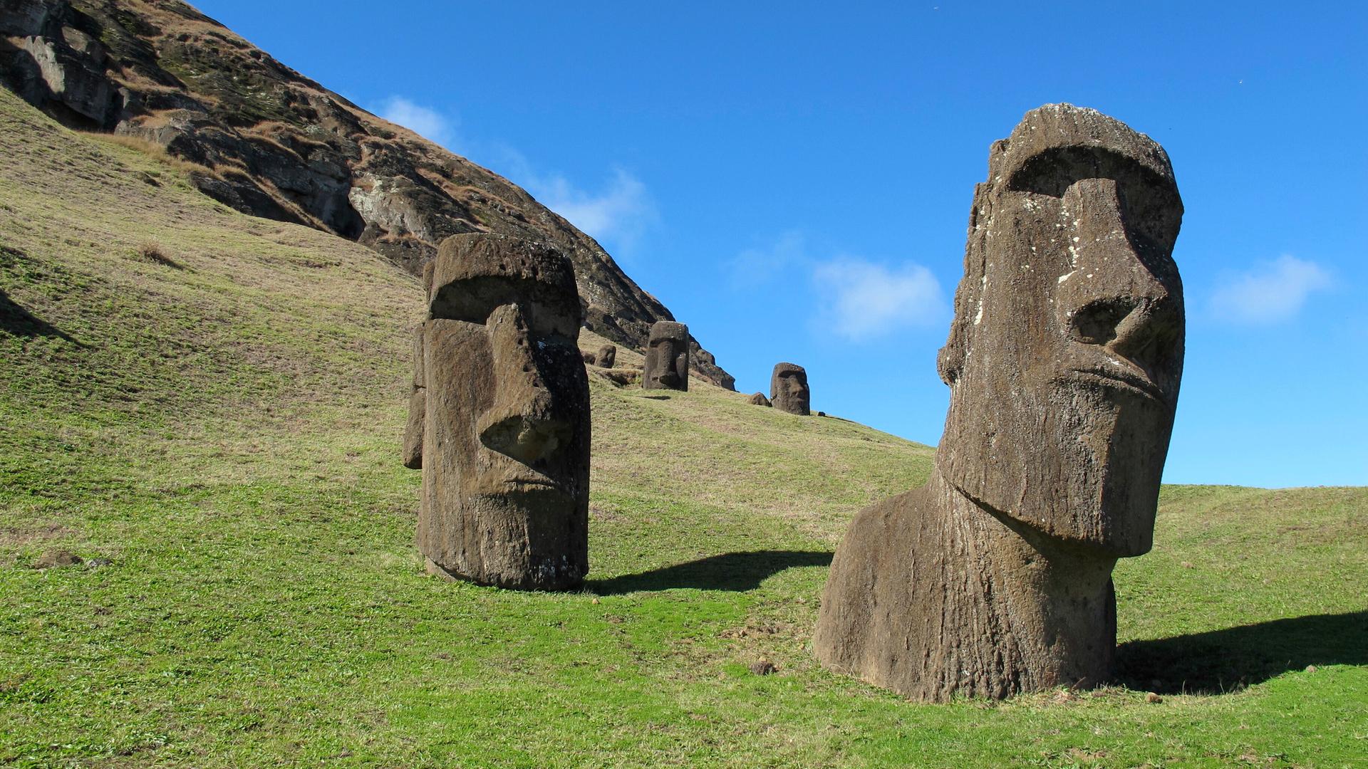 Die grauen Statuen stehen auf einer grünen Wiese vor einem felsigen Hang. Die grauen Statuen stehen auf einer grünen Wiese vor einem felsigen Hang.