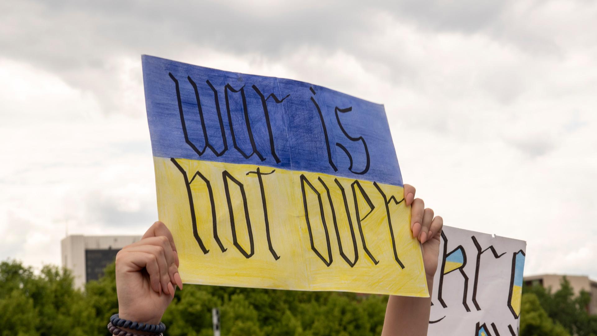 Eine Person hält vor dem Kanzleramt in Berlin ein Plakat mit der Aufschrift „War is not over“ in die Höhe. Eine Person hält vor dem Kanzleramt in Berlin ein Plakat mit der Aufschrift „War is not over“ in die Höhe.
