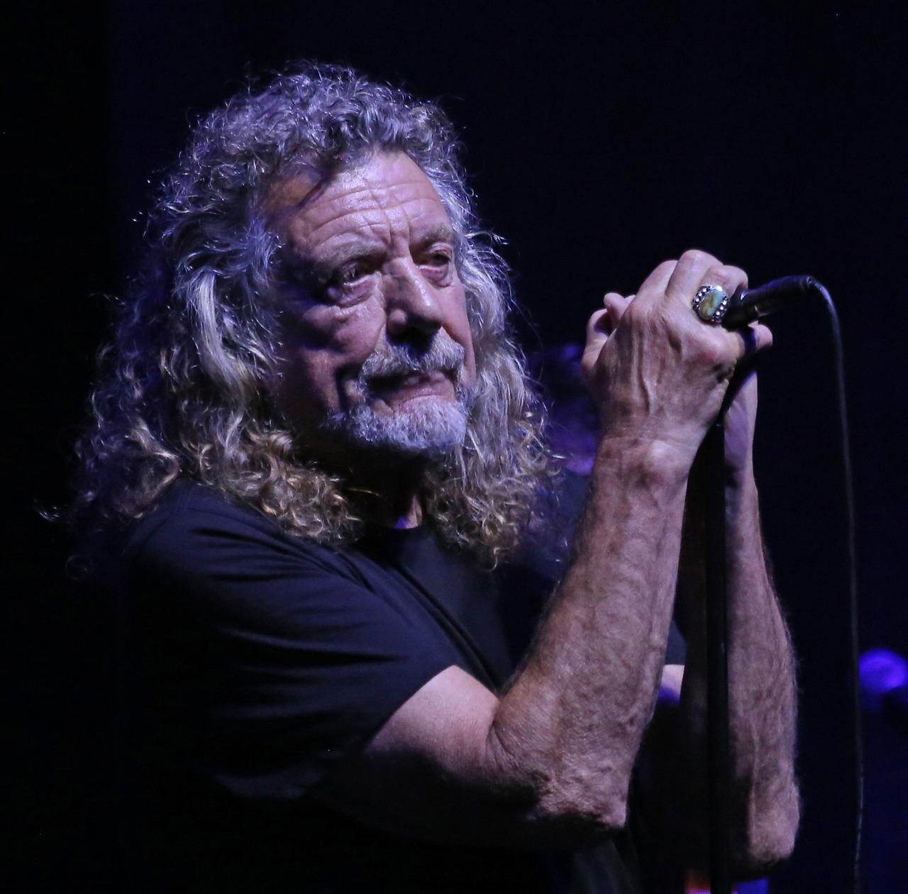 Robert Plant mit beiden Händen an einem Mikrofon vor schwarzem Hintergrund.