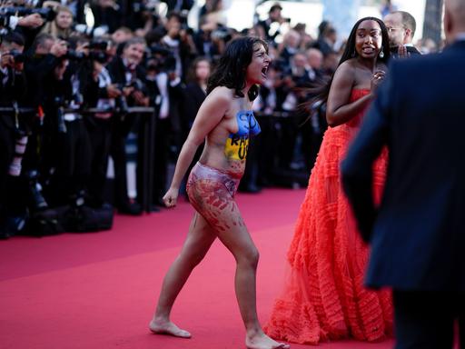 Eine Frau mit bemaltem Oberkörper stürmt den roten Teppich beim Filmfestival in Cannes.