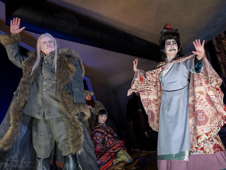 Ein Soldat im Wintermantel, zwei Frauen in chinesisch anmutenden Kleidern und ein Mann im Anzug stehen auf der Bühne.