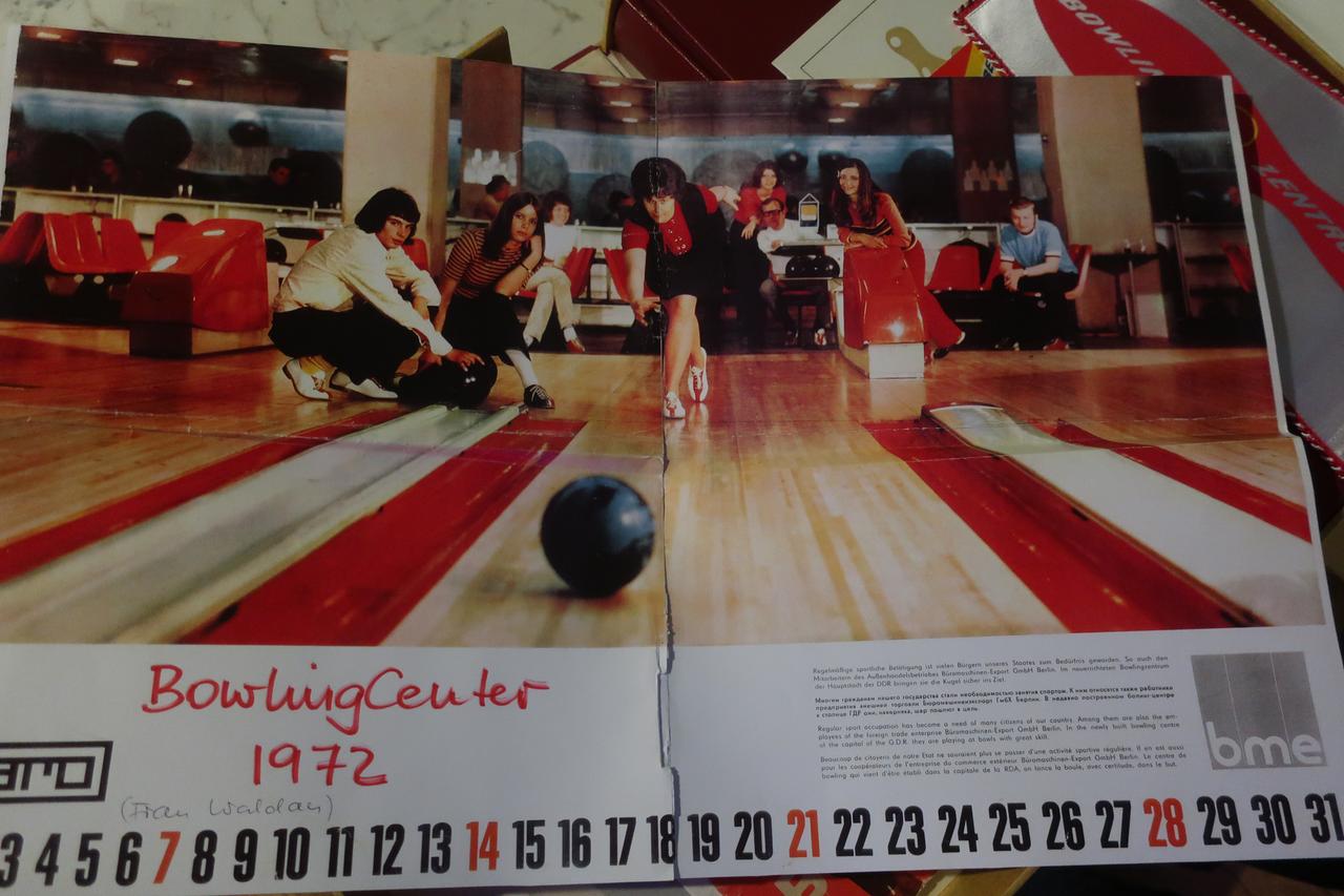 1970er-Jahre. Eine Frau lässt eine Bowlingkugel rollen, während neben der Bahn jugendliche in zeittypischen Klamotten begeistert zugucken. 1970er-Jahre. Eine Frau lässt eine Bowlingkugel rollen, während neben der Bahn jugendliche in zeittypischen Klamotten begeistert zugucken.