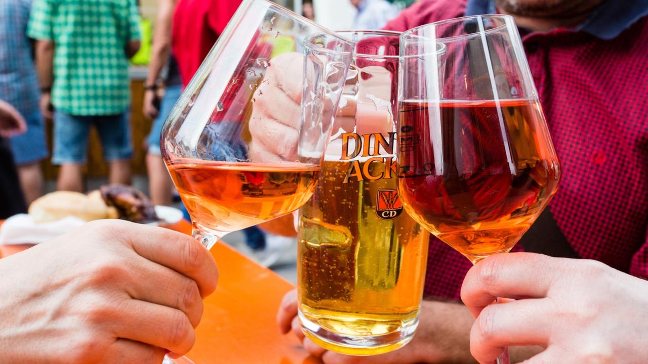 Drei Personen stoßen mit einem Glas Rotwein, Rose und Bier an.