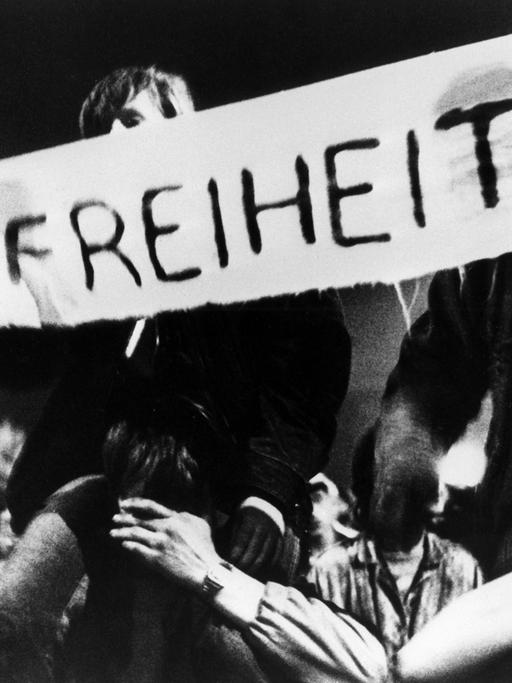 Zwei Männer, Teilnehmer des friedlichen Demonstrationszuges am 09.10.1989 durch die Leipziger Innenstadt, halten ein Banner mit der Aufschrift "Freiheit!"