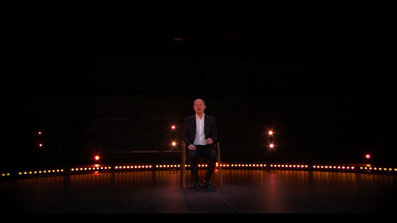 Der designierte Bundeskanzler Olaf Scholz sitzt in einem dunklen Fernsehstudio auf einem Stuhl und spricht. 