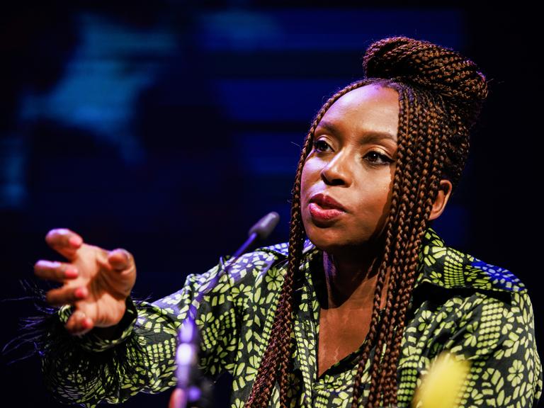 Chimamanda Ngozi Adichie spricht in ein Mikrofon und unterstreicht ihre Worte mit einer zupackenden Geste.