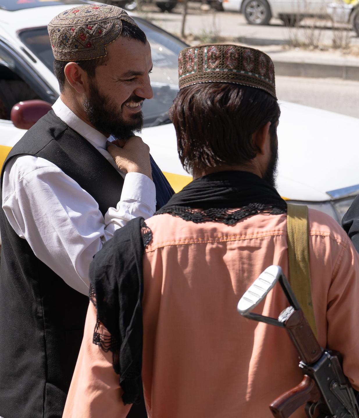 Zwei Männer mit paschtunischer Kappe - einer davon mit Bart, stehen vor einem Auto und unterhalten sich.
