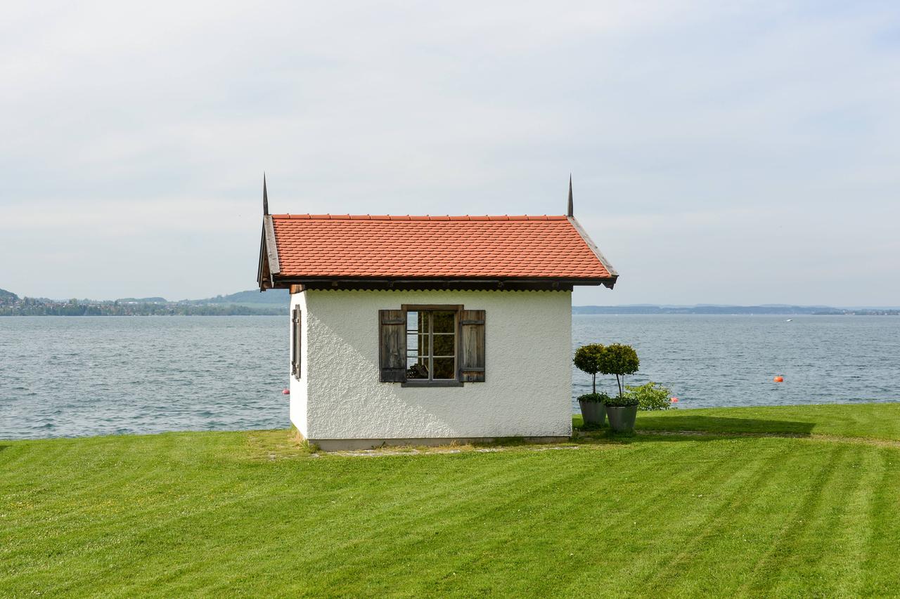 Ein winziges, weißes Häuschen mit Fensterläden steht direkt am Wasser eines großen Sees