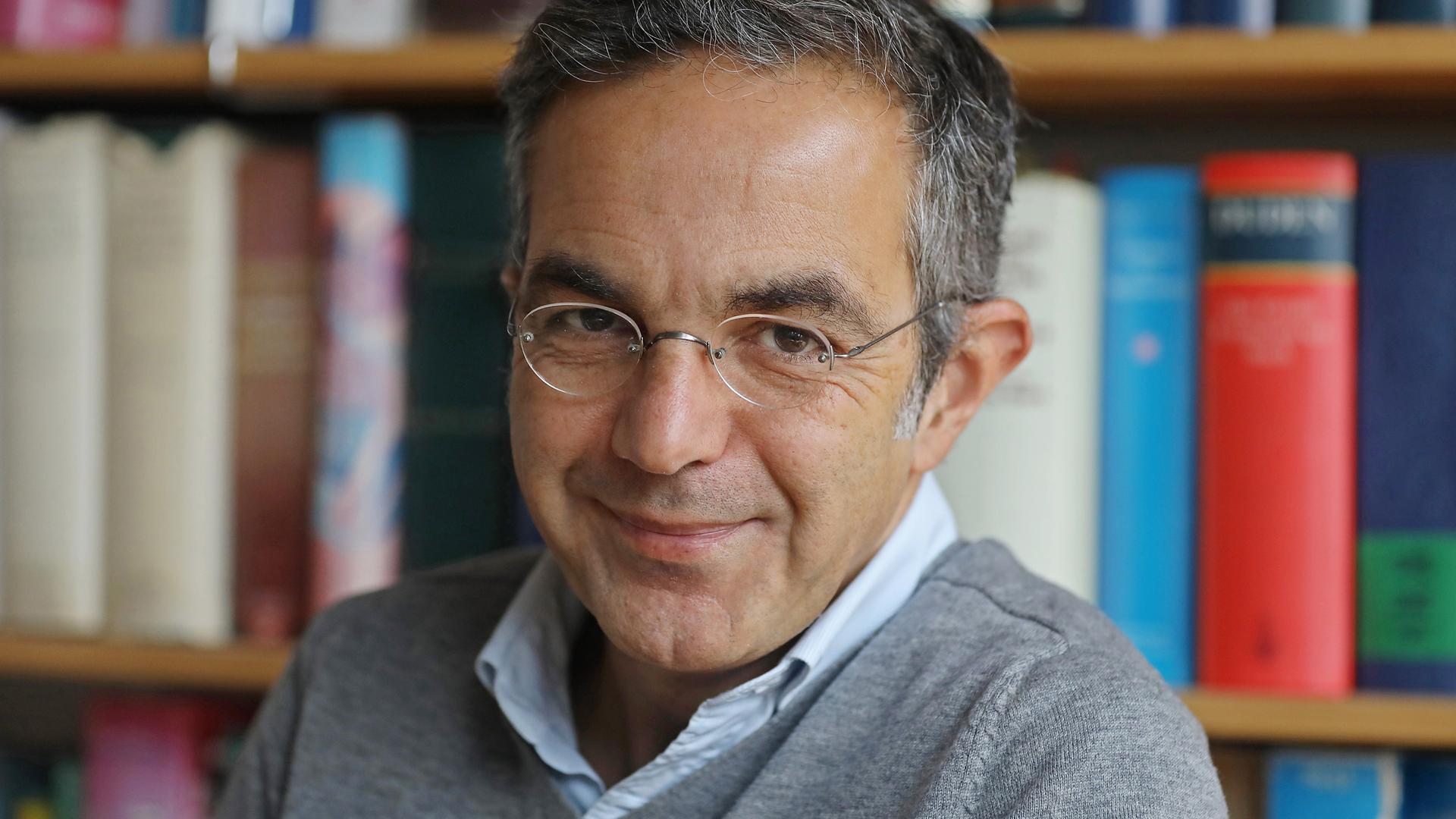 Navid Kermani sitzt lächelnd vor einem Bücherregal Navid Kermani sitzt lächelnd vor einem Bücherregal