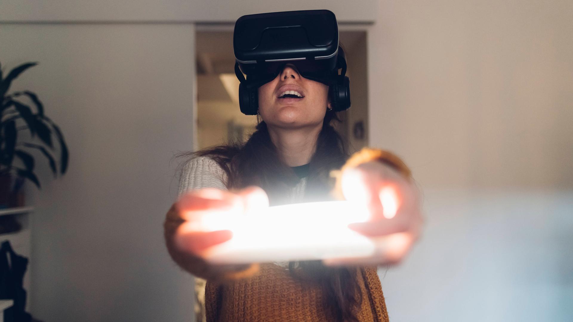 Eine Frau hält eine Virtual Reality Konsole und trägt Kopfhörer. Eine Frau hält eine Virtual Reality Konsole und trägt Kopfhörer.