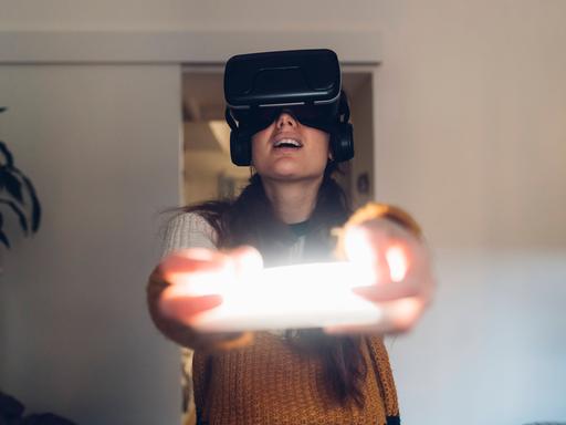 Eine Frau hält eine Virtual Reality Konsole und trägt Kopfhörer.