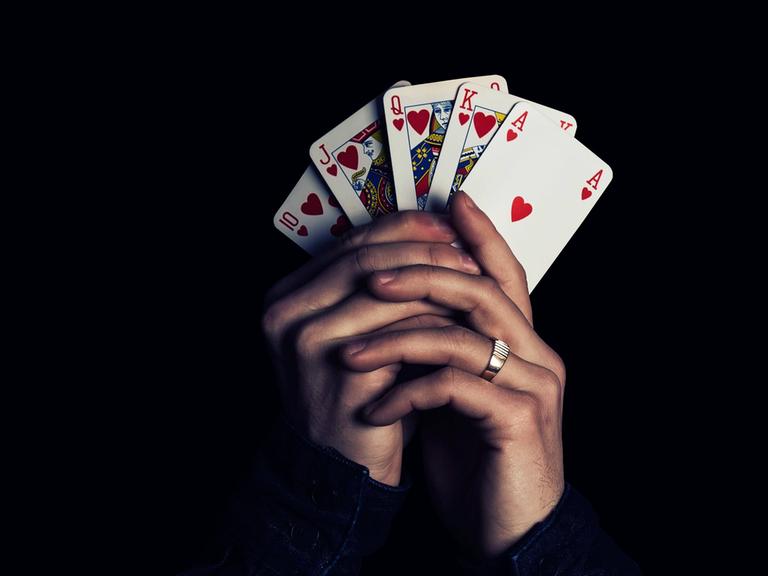 Zwei Hände fächern fünf Spielkarten auf und halten sie in die Kamera, Herz Zehn, Bube, Dame, König, Ass.