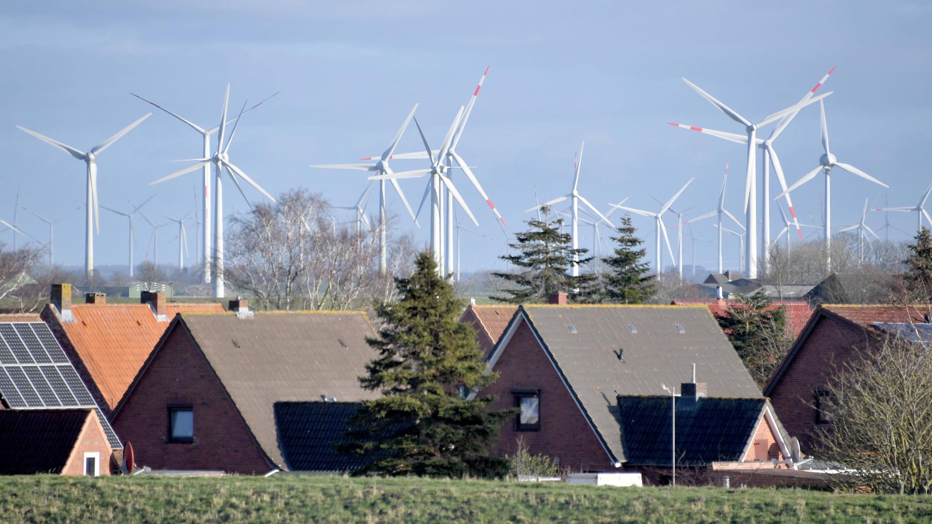 Mehrere Windkraftanlagen sind hinter einer Wohnsiedlung zu sehen.