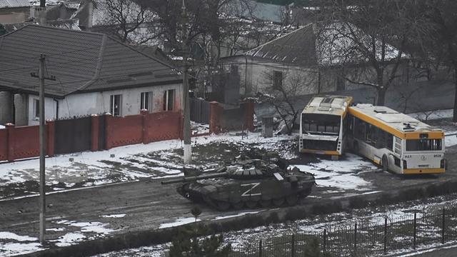 Ein Panzer der russischen Armee mit einem "Z" an der Seite bewegt sich durch eine Straße am Stadtrand von Mariupol, Ukraine. Daneben sind zwei zerstörte Busse zu sehen. 