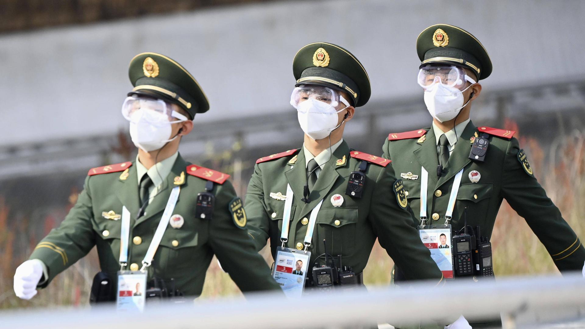 Drei Polizisten der Volksrepublik China marschieren durch ein Veranstaltungsort der Olympischen Winterspiele 2022 in Peking. Sie tragen grüne Uniformen und weiße Masken. Drei Polizisten der Volksrepublik China marschieren durch ein Veranstaltungsort der Olympischen Winterspiele 2022 in Peking. Sie tragen grüne Uniformen und weiße Masken.
