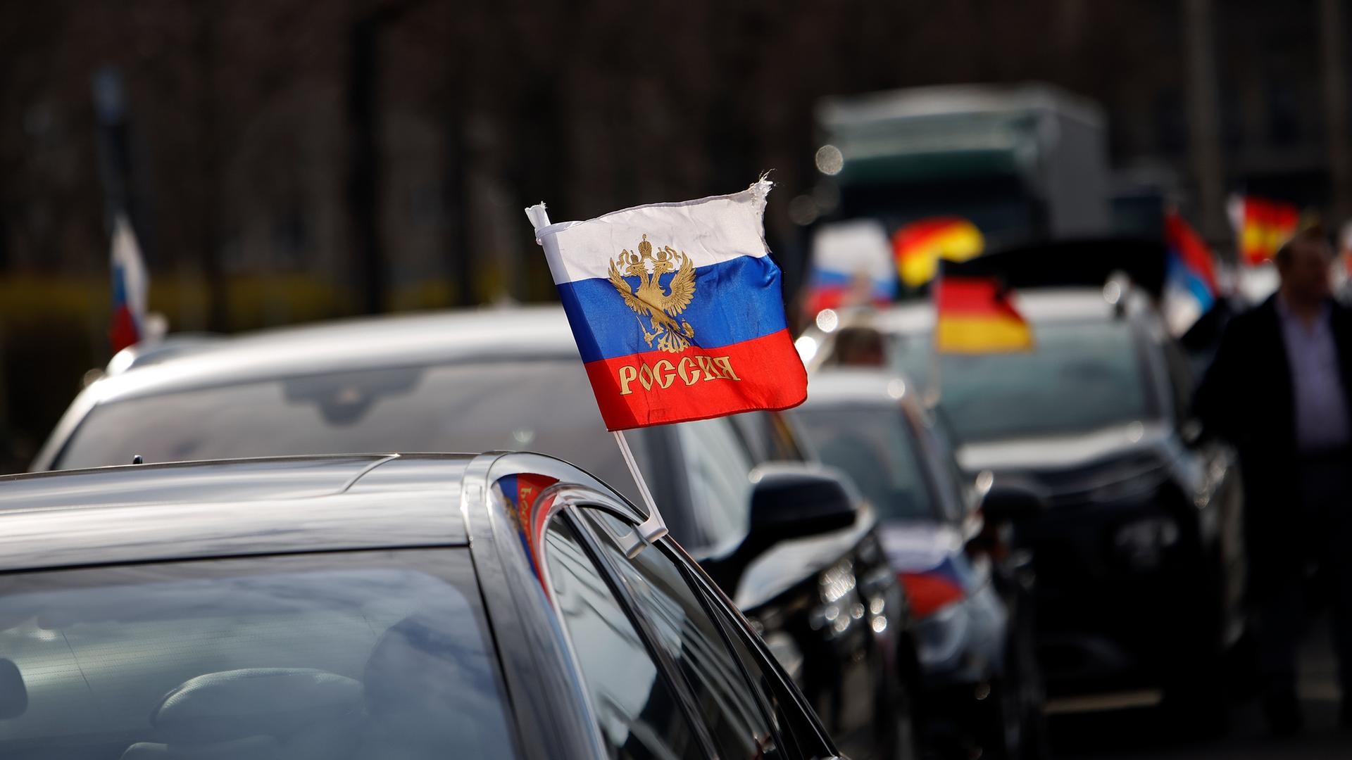Flaggen mit den russischen Nationalfarben und dem russischen Staatswappen wehen an einem Auto auf dem Olympiaplatz vor dem Olympiastadion. Etwa 900 Menschen haben am Sonntag in Berlin an einem Autokorso mit russischen Fahnen teilgenommen. Flaggen mit den russischen Nationalfarben und dem russischen Staatswappen wehen an einem Auto auf dem Olympiaplatz vor dem Olympiastadion. Etwa 900 Menschen haben am Sonntag in Berlin an einem Autokorso mit russischen Fahnen teilgenommen.