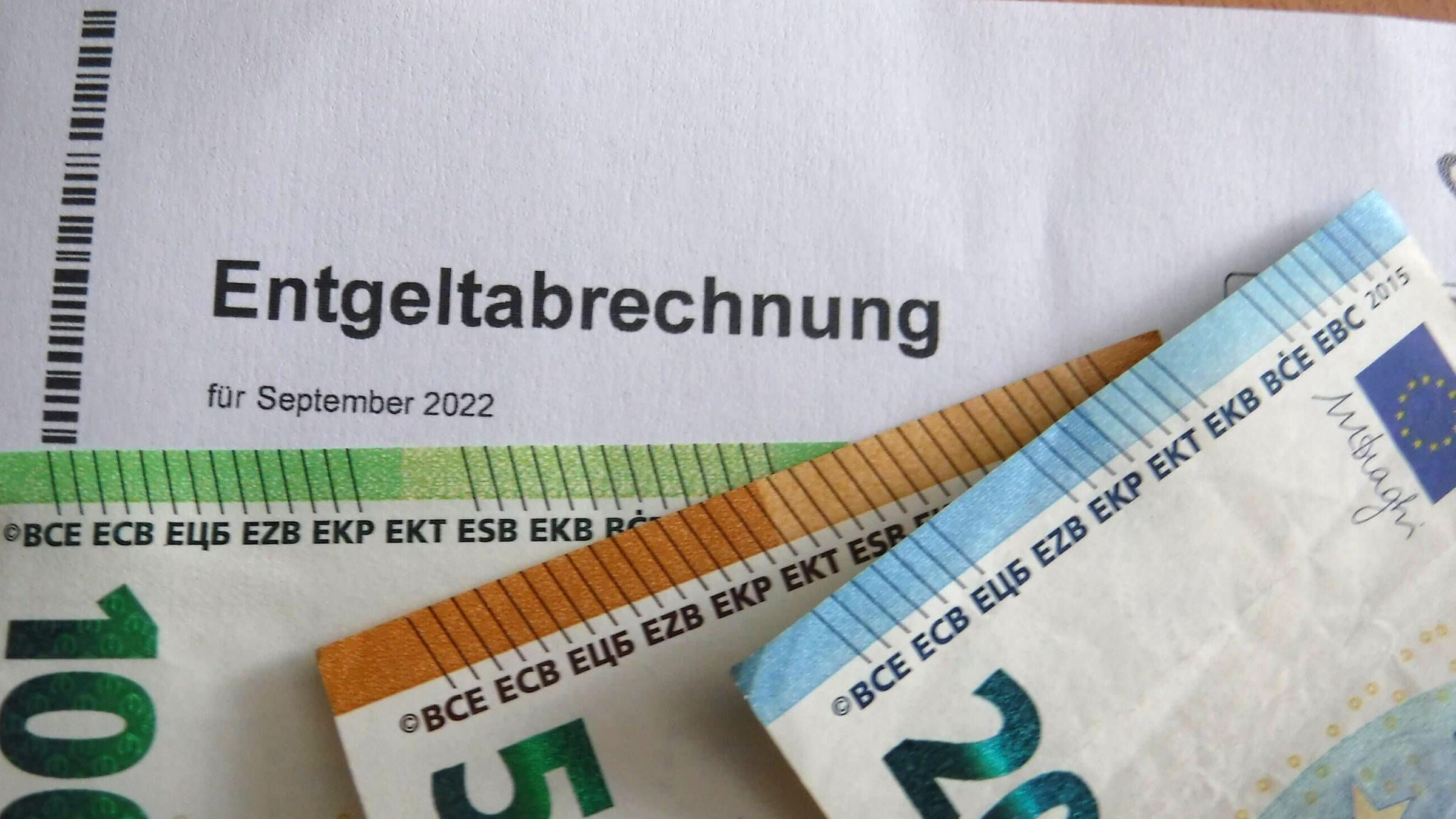 Auf einer Lohnabrechnung vom September 2022 liegen mehrere Geldscheine Auf einer Lohnabrechnung vom September 2022 liegen mehrere Geldscheine