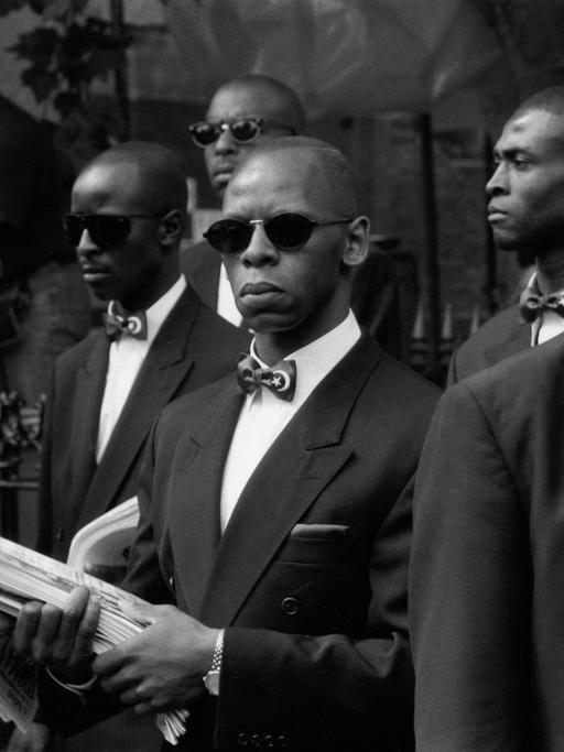 Mitglieder der 'Nation of Islam' stehen in ihren Anzügen und mit schwarzen Sonnenbrillen in Notting Hill auf der Straße mit ihrer Mitgliederzeitschrift 1991.